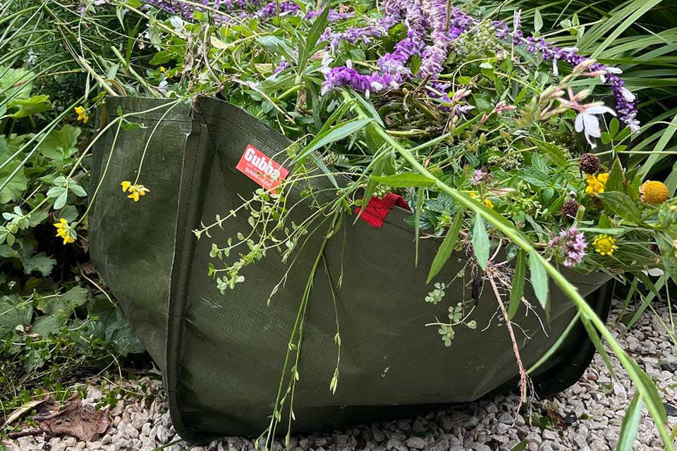 Green fabric planter with purple flowers and greenery in a garden setting