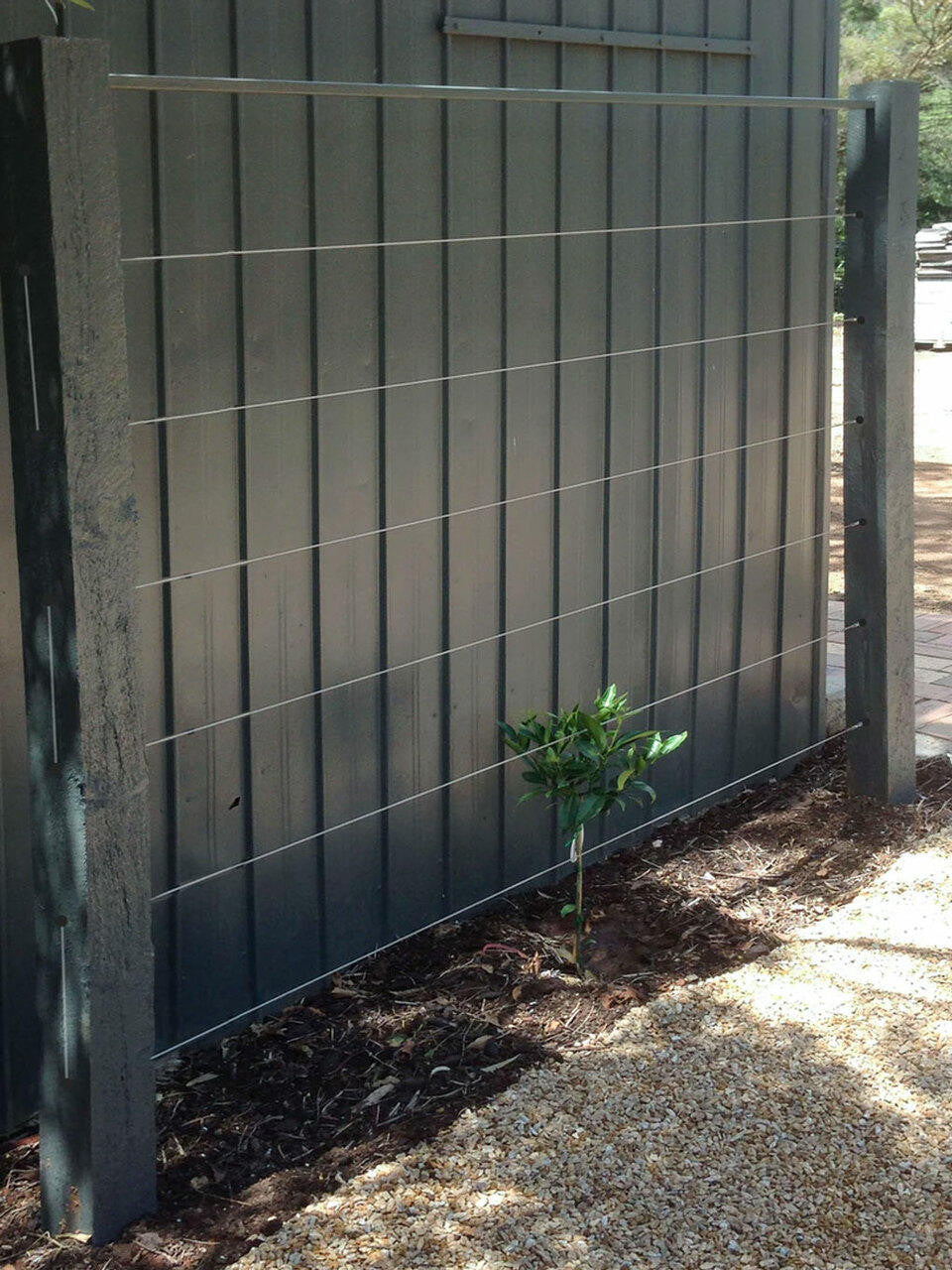 Post mounted espalier kit with wire by Espalar, featuring wooden posts and metal wires for garden fruit tree training.